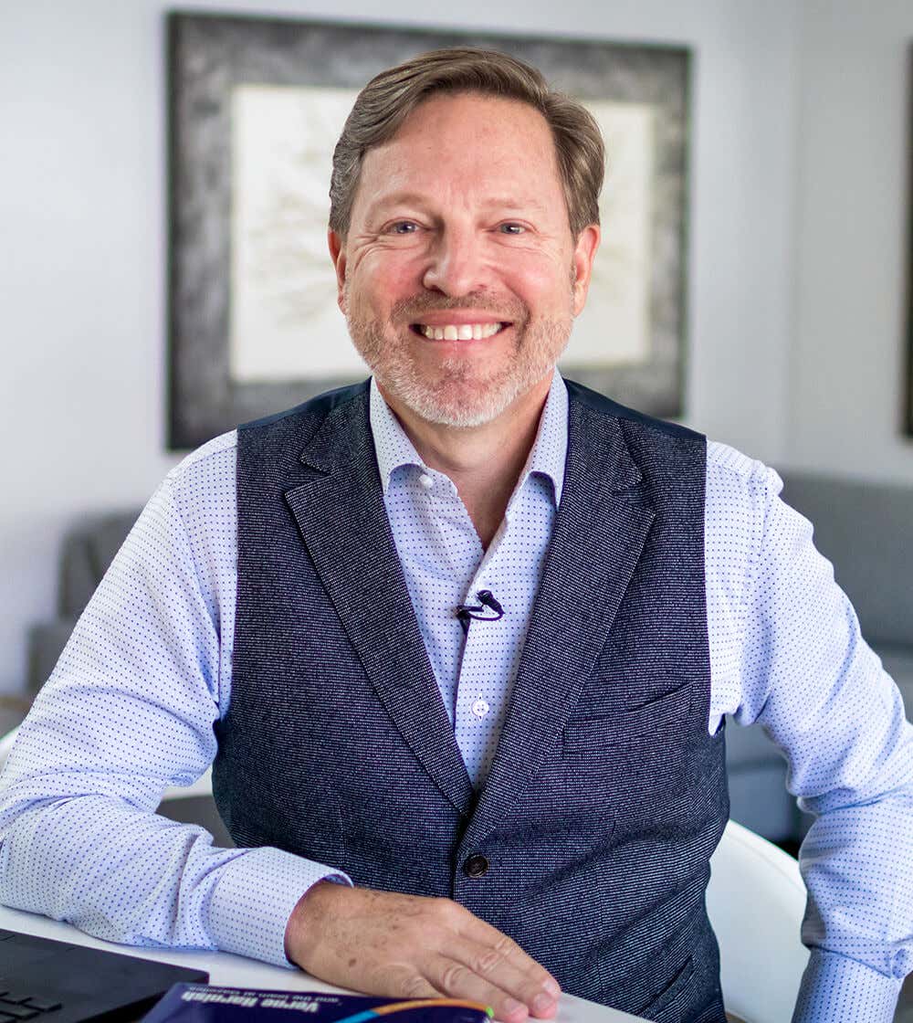 Verne smiling, wearing a dark gray waistcoat on top of a light blue shirt