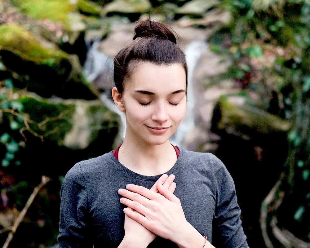 Women standing in nature, placing both hands on her chest