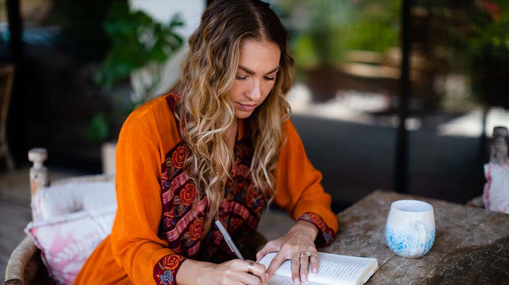 Rachel wearing pink top, overlayed with a white cardigan, reading her "Wild Open" book