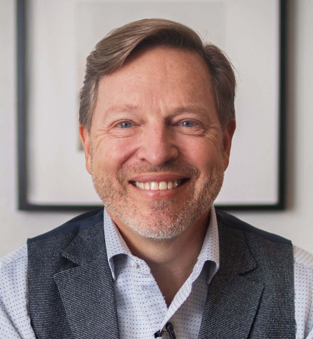 Verne wearing a floral blue shirt and suit, front-facing and smiling.