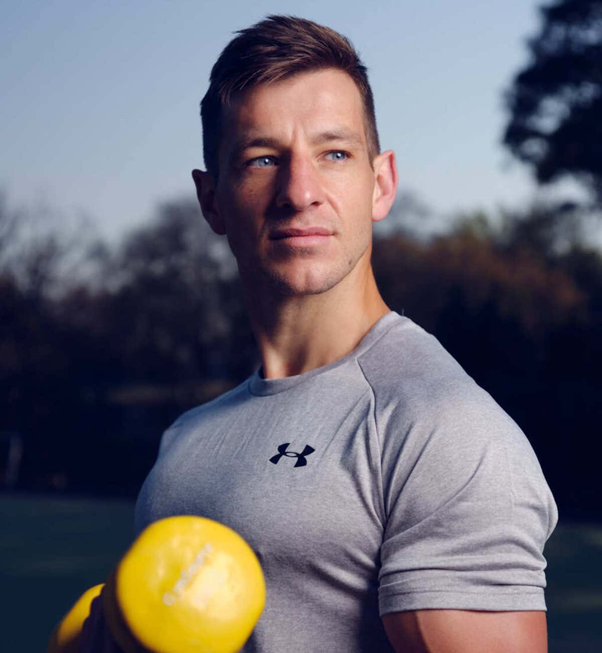 Lorenzo wearing a gray under armour t-shirt, carrying a yellow dumbell.