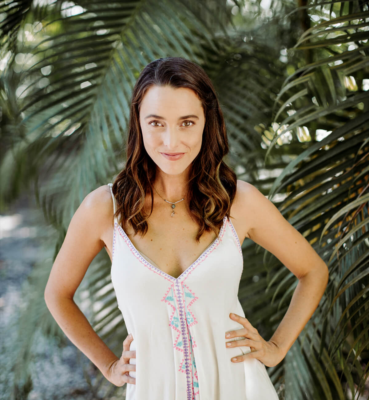 Jennifer Partridge front facing, wearing a white bohemian dress with a lush greenery backdrop