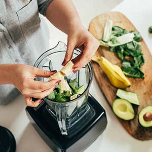 Top view of a juice blender, with avocados, bananas and leafy greens.