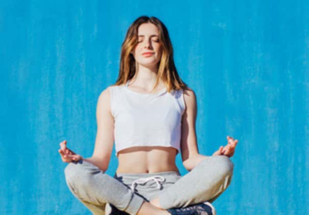 Young woman doing lotus position in front of a colorful wal