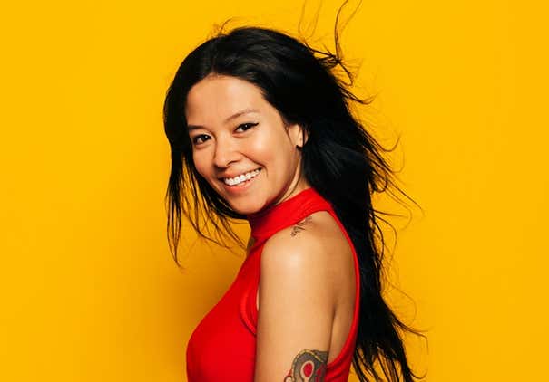 Happy young asian woman laughing over yellow background. She is wearing a red shirt and looking at camera
