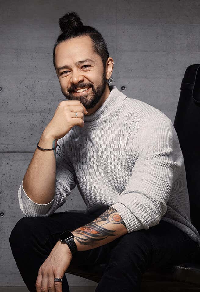 Ronan en fondo morado sonriendo y con los brazos cruzados