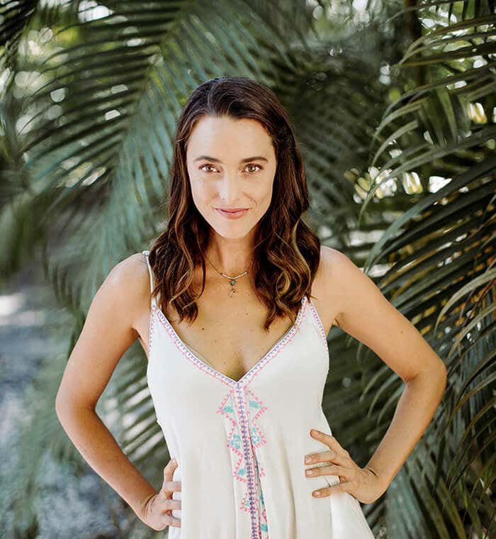 Jennifer Partridge front facing, wearing a white bohemian dress with a lush greenery backdrop