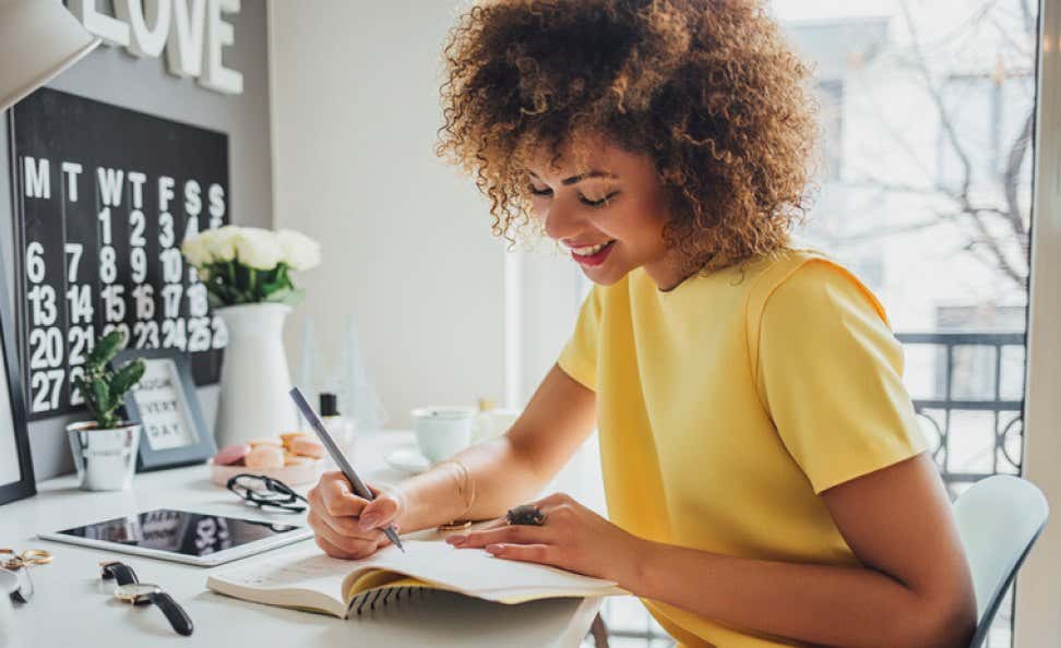 African woman sitting at her desk and writing in her Lifebook notebook wearing a yellow dress